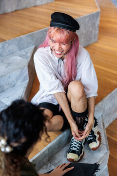 Pink-haired person laughs while sitting on stairs with another person