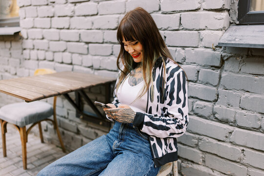 Young Woman Sits at a Table With Phone Outside in the City