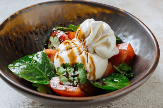 Burrata with tomatoes, greens, and balsamic drizzle in bowl 
