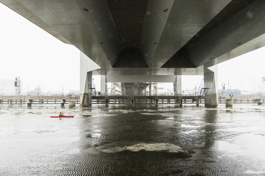 Red Kayak Navigating Through Ice Floes Under Large Urban Bridge
