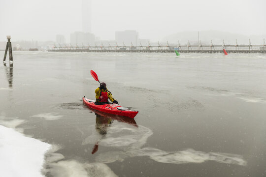 Kayaker Waving Paddle While Navigating Icy City Bay