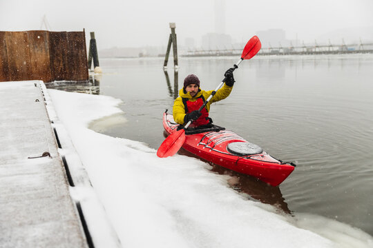 Kayaker Waving Paddle While Navigating Icy City Bay