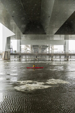 Red Kayak Navigating Through Ice Floes Under Large Urban Bridge