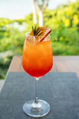 Refreshing orange cocktail spritz in a wine glass garnished with orange slice and rosemary. Set on a table with a blurred green garden background. Perfect for summer travel and leisure themes. © Yellow Boat
