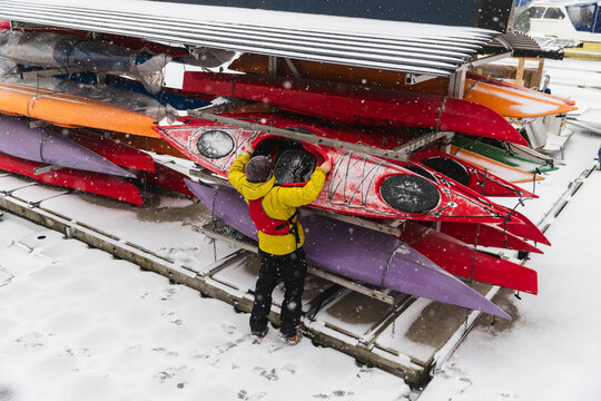 Adventurer Selecting Red Kayak from Snowy Outdoor Storage Rack