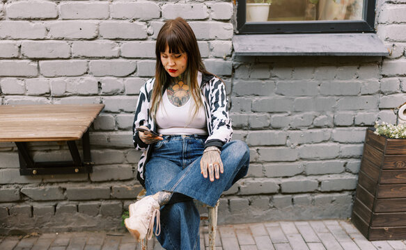 Young Woman Sitting in a Cafe Checking Her Phone in Urban Setting