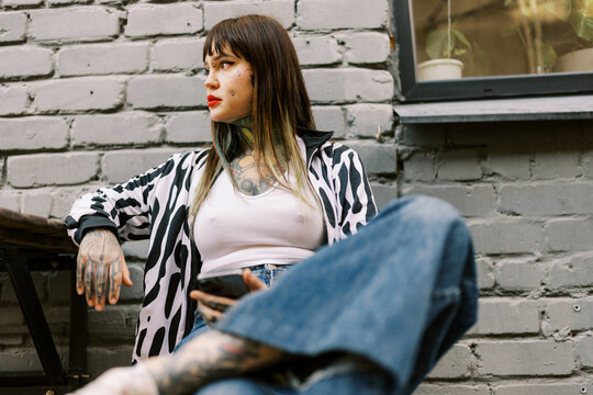 Woman Sits on Ground With Phone in Hand Near Gray Brick Wall