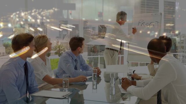 Presenter writing profit then success on flip-chart, starting city-light overlay while team noting