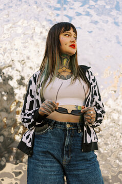 Young Woman With Tattoos Stands Confidently in Front of Shiny Surface