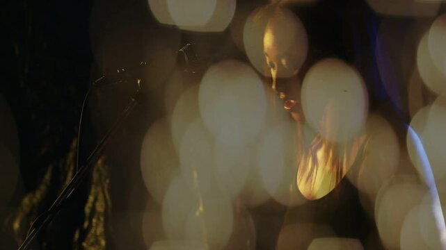 Singer pressing first key and leaning to mic, singing as warm bokeh lights floating for audience