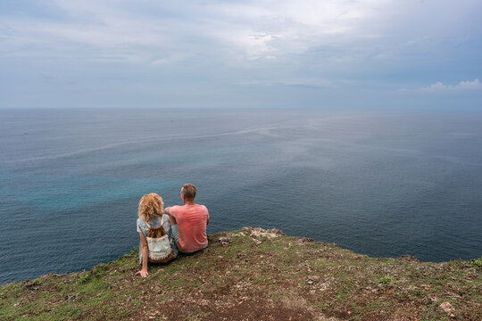 Couple Sitting on Coastal Cliff Overlooking Calm Ocean