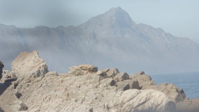 Camera moving near sheer screen, bands drifting across rocky coast, revealing distant peak for film