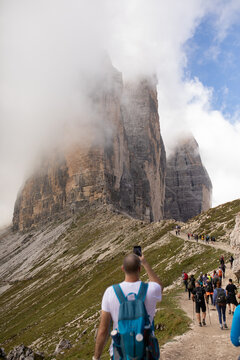 A hiker takes a photo of the Tre Cime peaks using their phone, Italy