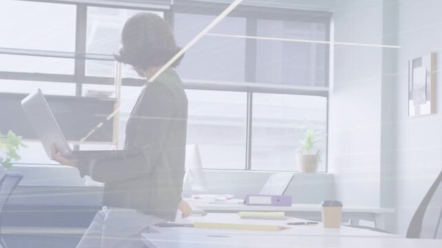 Woman standing at desk opening binder flipping pages leaning checking laptop reviewing for business