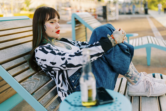 Woman Sits on Bench While Enjoying Drink and Relaxing Outdoors