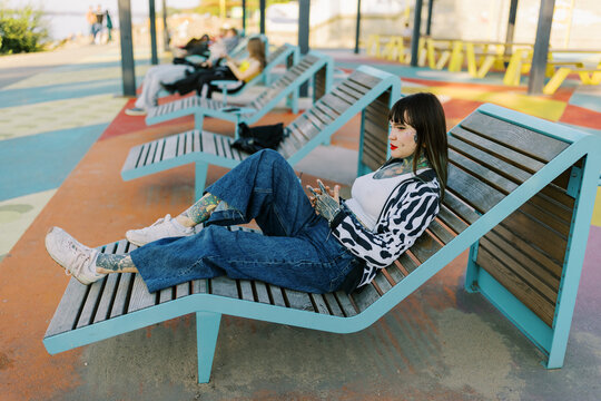 Young Woman Sits on Bench in Outdoor Area While Using Phone