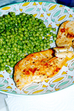 a grilled chicken breast with green peas on a patterned plate
