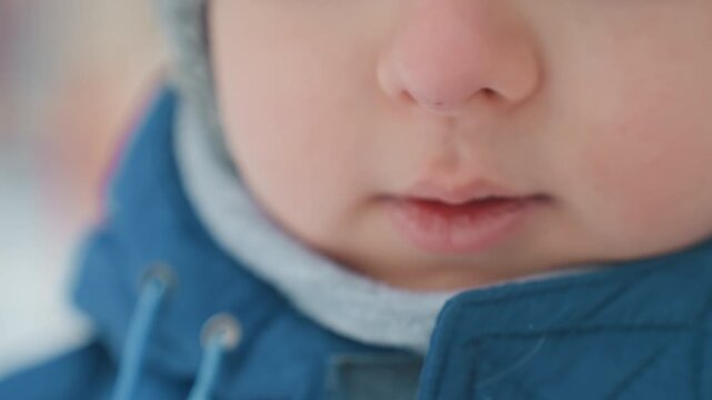 Young son blowing soap bubble outdoors, bundled in blue winter jacket with knit hat and scarf, closeup on lips and breath forming fragile bubble, soft frosty light and blurred snowy background, candid