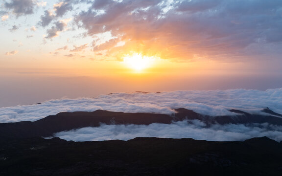 Aerial view of Bica da Cana at sunset with golden sun rays shining over a sea of clouds and dark mountain ridges in Ponta do Sol, Madeira, Portugal.
