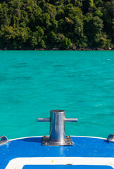 Fototapeta premium Bow bollard on boat facing tropical island. Turquoise sea in the background. Lush green forested coastline.