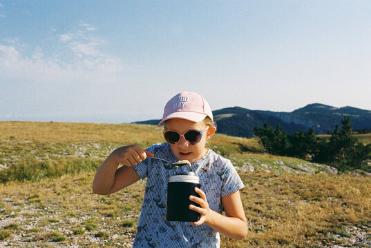 A teenager girl eats hot food from a thermos on a hike.