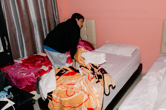 Man making a bed in a hotel room during a surfing trip to Morocco