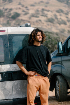Bearded man with curly hair, standing firmly behind a van
