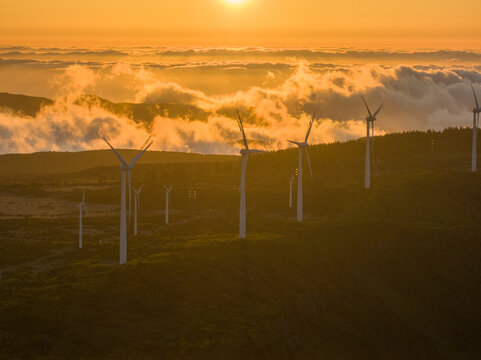 Aerial view of wind turbines at Bica da Cana on a mountain ridge above a sea of clouds during golden hour in Ponta do Sol, Madeira, Portugal.