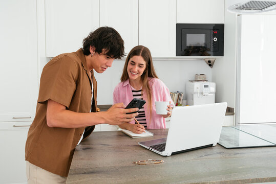 Young Couple Managing Finances with Smartphone and Laptop at Home