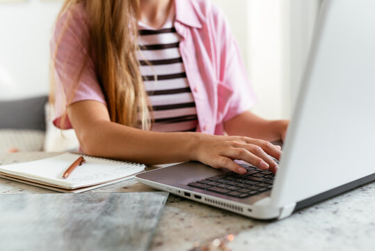 Anonymous young woman using laptop and taking notes
