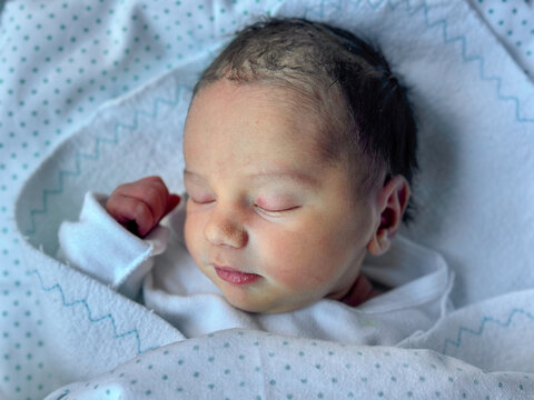 Closeup Of Newborn Baby Sleeping Wrapped In Hospital Blanket