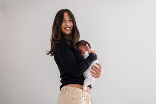 Smiling Woman Holding her Newborn Baby Against Her Chest At Home