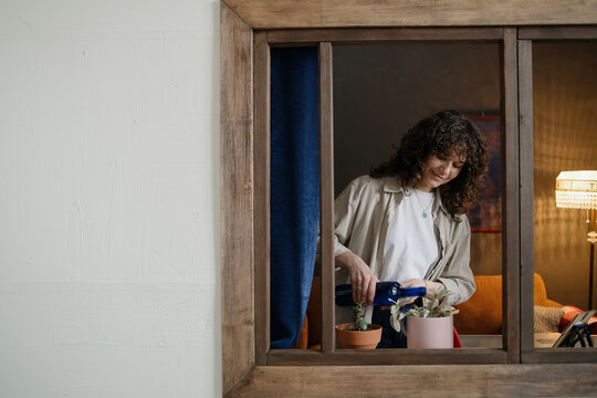 Woman watering plants on windowsill with glass bottle