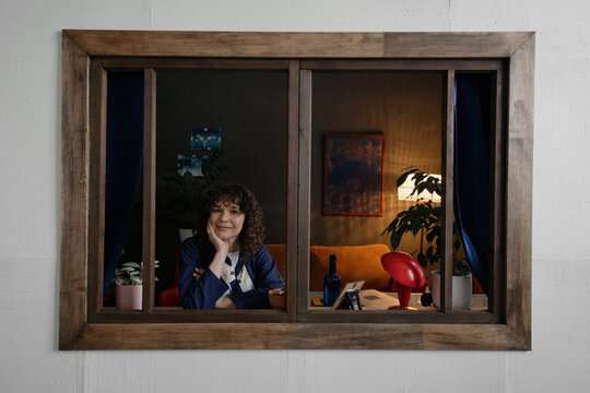 Curly-haired woman looking at camera from her home, view from outside