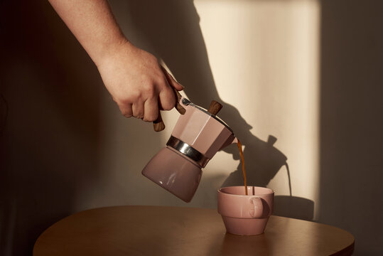 Pouring coffee from a moka pot into a pink cup 