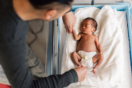 Father holding newborn baby hand in hospital bassinet