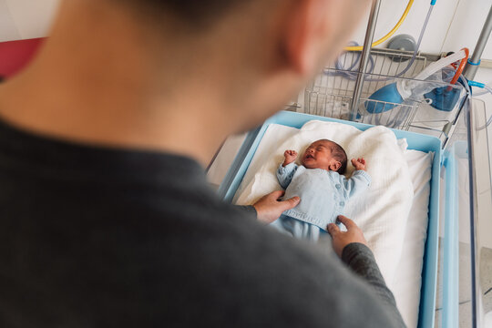 Father comforting newborn baby in hospital bassinet