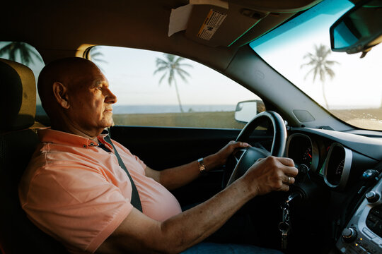 Elderly Man Driving a Car by the Beach During Sunset
