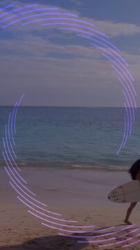 Vertical video: Appearing purple arc, surfer in bikini walking beach to surf with board, copy space