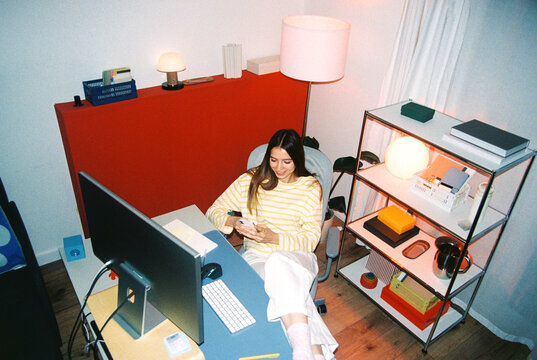 Woman using smartphone at desk in home office film photo