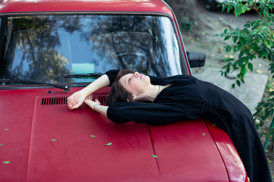 Portrait of a young woman in a black dress near a cherry-colored car