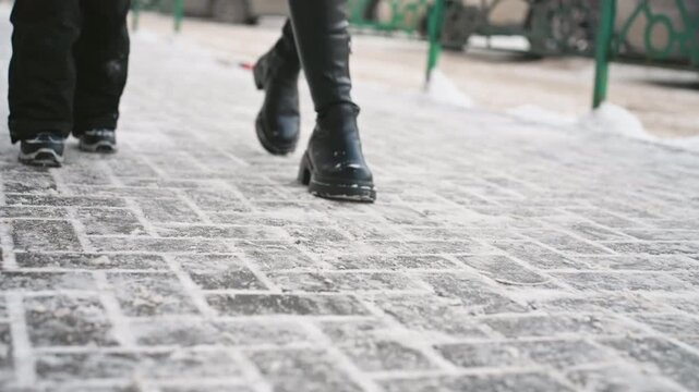 Icy cobblestone street white mom and son, commuter mom striding with purpose while child follows in warm coat and snow boots, textured paving dusted with snow, parked cars and green railing