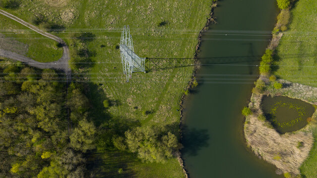 Aerial view of a high-voltage electricity pylon and power lines crossing a river and green fields near the RWE Power AG power plant Gersteinwerk in Werne, Nordrhein-Westfalen, Germany.