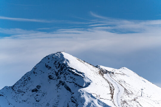 Snowy mountain peak with ski piste under blue cloudy sky