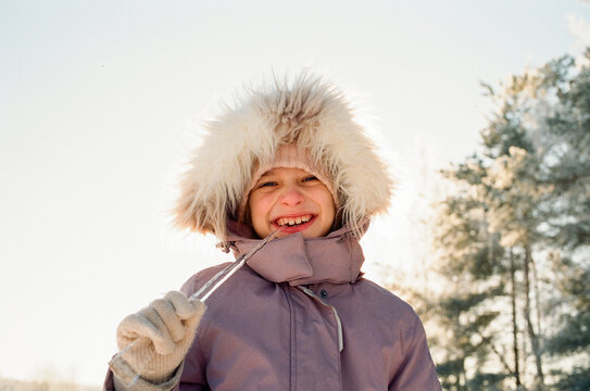 Smiling Child in Fur Hood Biting Ice on Sunny Winter Day