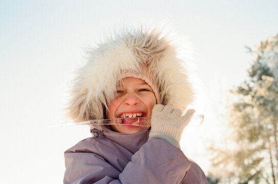 Smiling Child in Winter Clothing Biting Ice Outdoors