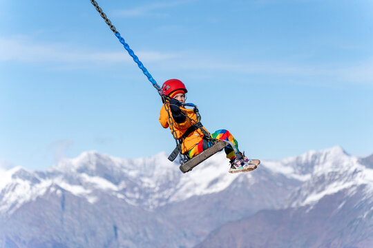 Child swings on ropes over snowy mountains against blue sky