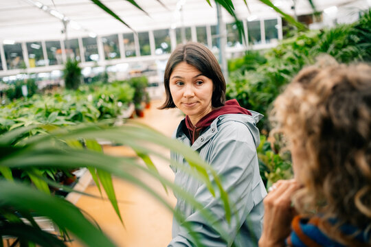 Woman Talks to Friend in Plant Store in Bright Greenhouse