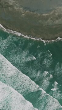 Aerial view of powerful waves crashing onto a black sand beach Marokopa, Waikato, New Zealand. The raw beauty of nature's force is on full display.