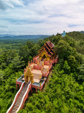 Aerial view of Wat Phra That Doi Phra Chan temple with its golden architecture and long staircase surrounded by lush green forest in Tambon Pa Tan, Chang Wat Lampang, Thailand.